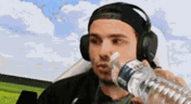 a man wearing headphones is drinking water from a plastic bottle .