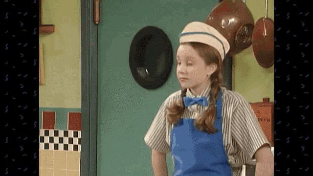 a girl in a kitchen wearing a hat and apron