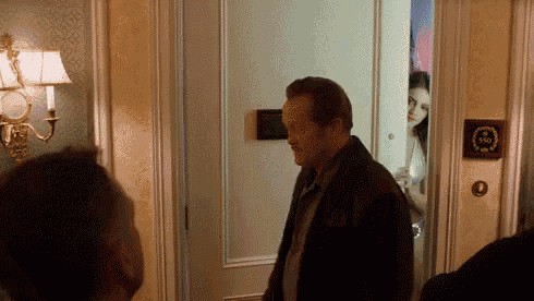 a man in a brown jacket is standing in a doorway looking at a woman behind him .