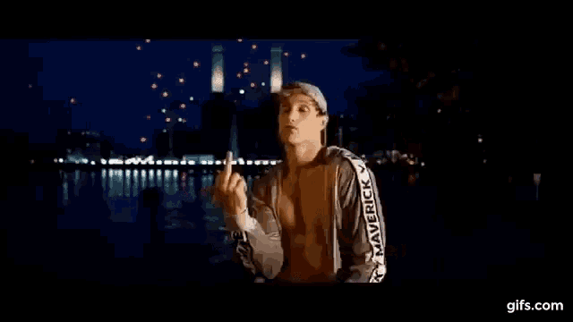 a man without a shirt is giving the middle finger in front of a river .
