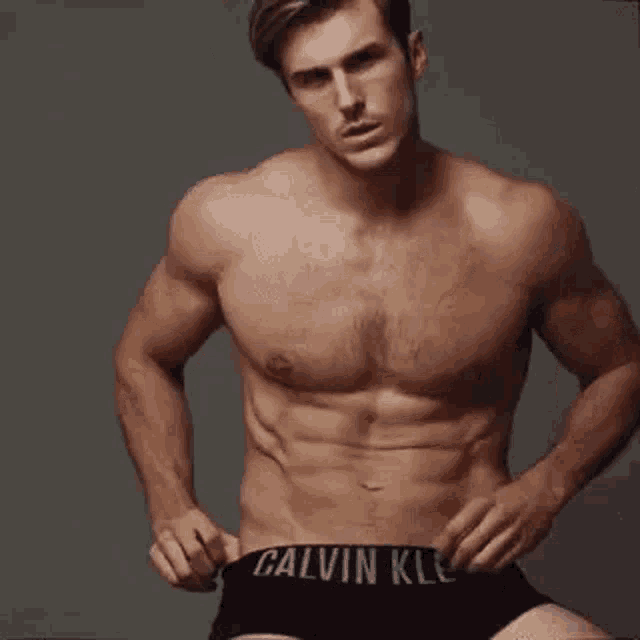 a shirtless man in black underwear is standing in front of a gray wall .