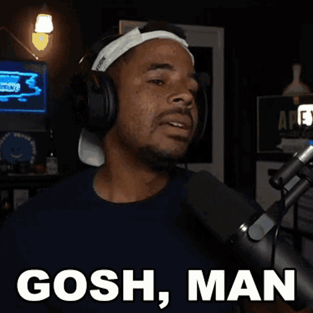 a man wearing headphones and a headband is talking into a microphone and saying gosh man