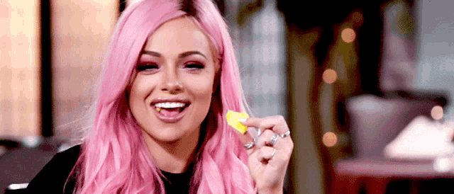a woman with pink hair is smiling while eating a piece of food .