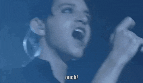 a man is singing into a microphone with the words ouch written on the bottom of the screen .