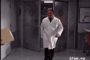 a man in a lab coat is walking through a hallway .
