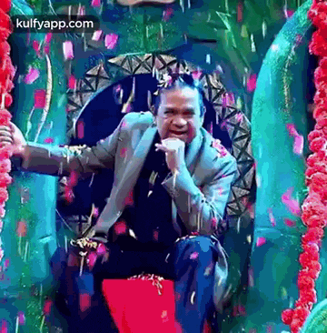 a man in a suit is sitting on a red throne with confetti falling around him .