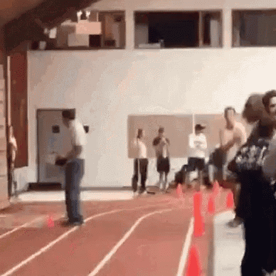a group of people are standing on a track in a gym watching a person run .