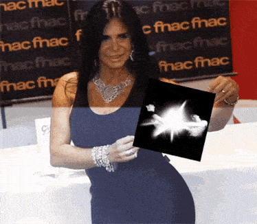 a woman in a black dress holds up a black and white photo in front of a sign that says fnac