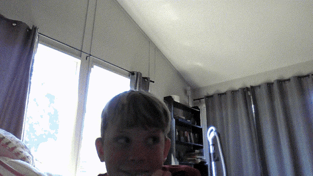 a young boy is sitting in front of a window with a bookshelf in the background
