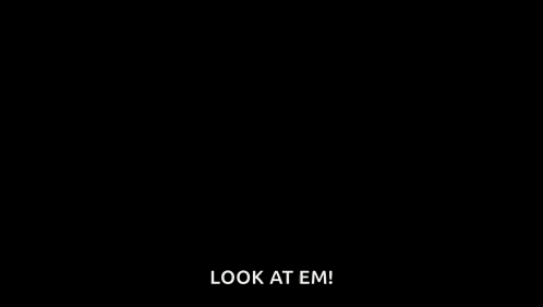 a person in a hoodie with red eyes is standing in the dark and says `` look at em '' .