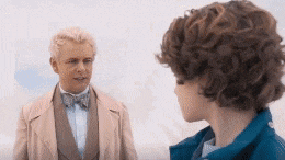 a man in a tuxedo and bow tie is talking to a young boy with curly hair .