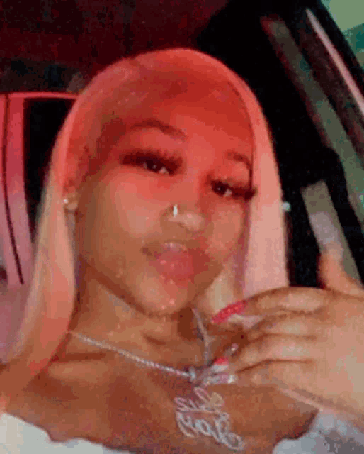a woman with long blonde hair is sitting in a car wearing a necklace and giving a thumbs up .