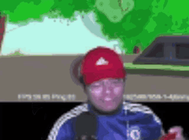 a man wearing a red hat and a blue jacket is standing in front of a green car .