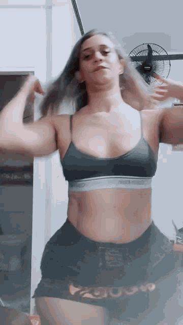 a woman in a crop top and shorts is standing in front of a ceiling fan .