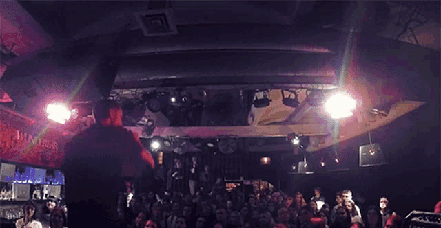 a man stands on stage in front of a crowd in a winterbar