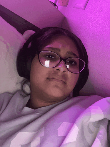 a girl wearing glasses and headphones is laying in bed