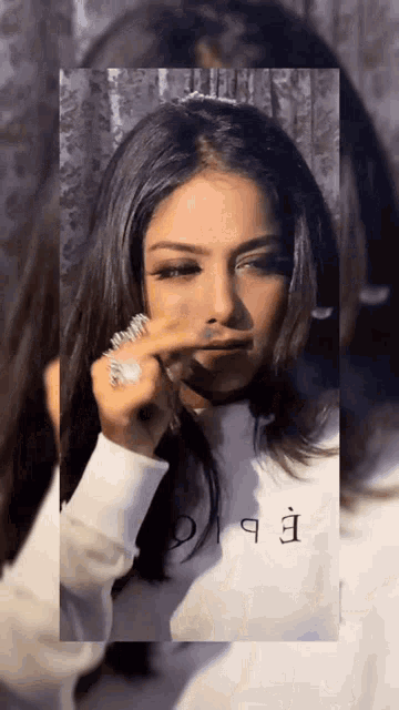 a woman wearing a white shirt with the letter e on it wipes her nose