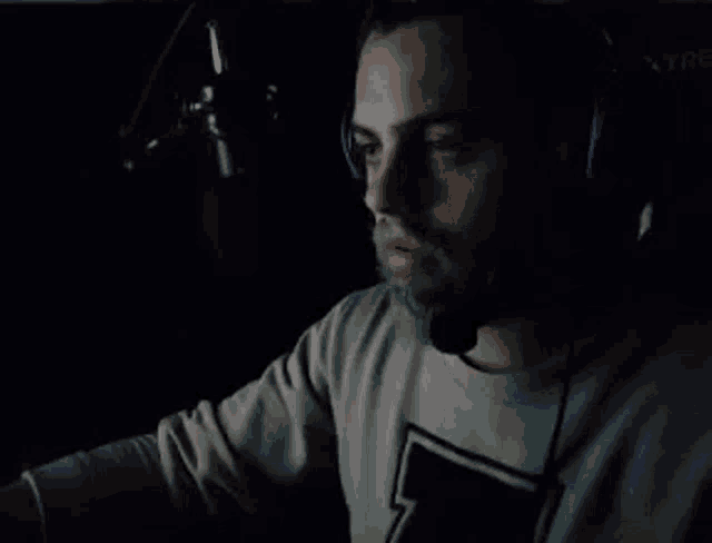 a man wearing headphones and a microphone is sitting in front of a microphone in a dark room .