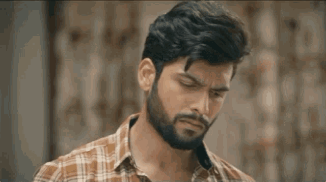 a man with a beard wearing a plaid shirt is looking to the side .