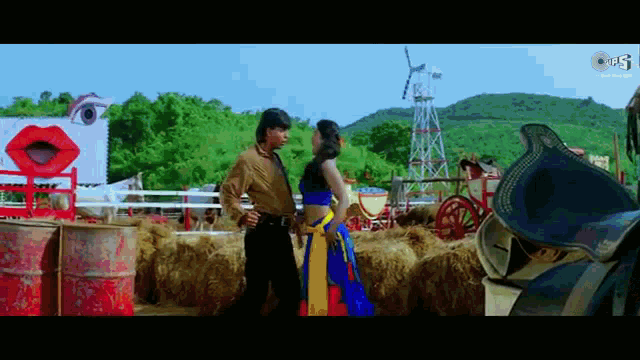a man and a woman are standing next to each other in front of a hay bale in a field .