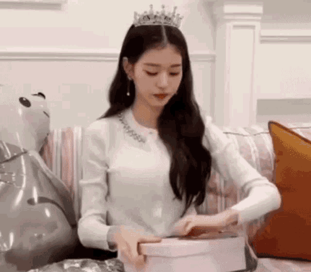 a woman wearing a tiara is sitting on a couch holding a pink box .