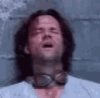 a man with glasses around his neck is laying down with his mouth open .