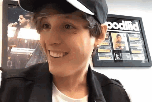 a young man wearing a black hat is smiling in front of a framed poster that says podlid