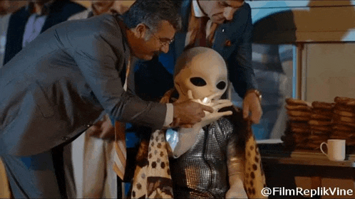 a man in a suit and tie is touching an alien 's face .