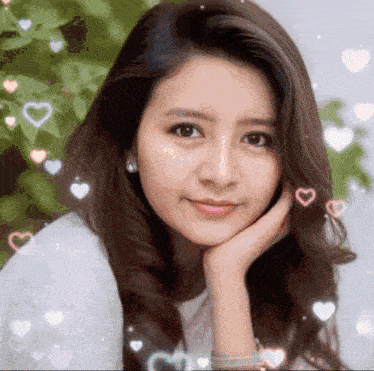 a close up of a woman 's face with her hand on her chin and hearts flying around her .
