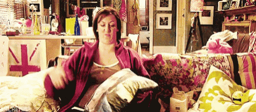 a woman is sitting on a couch holding a pillow and a book .