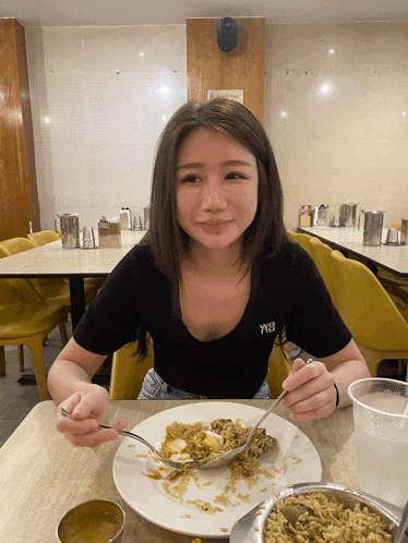 a woman sitting at a table with a plate of food and a spoon in her hand with a shirt that says y3