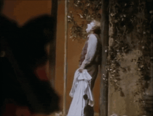 a man in a white shirt is standing in front of a wall holding a white cloth .