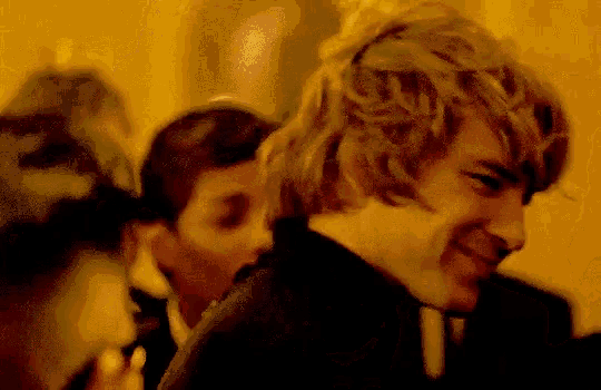 a man with curly hair is smiling in a blurry photo