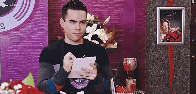 a man writes on a piece of paper in front of a framed picture of a woman with the word loveflora on it