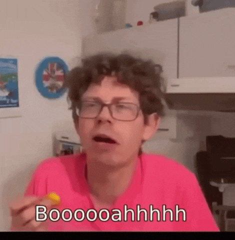 a man wearing glasses and a pink shirt is eating a yellow item and saying booooahhhh .