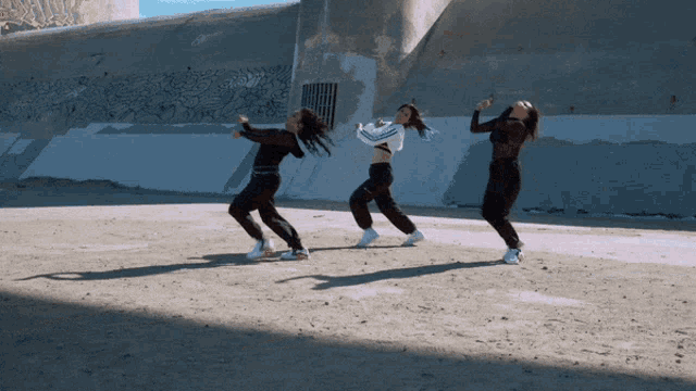 a group of women are dancing in front of a wall with graffiti on it