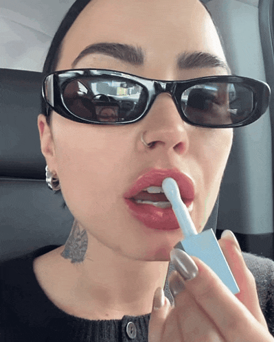 a woman wearing sunglasses is applying lipstick
