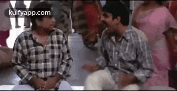 two men are sitting next to each other talking in a crowded room .