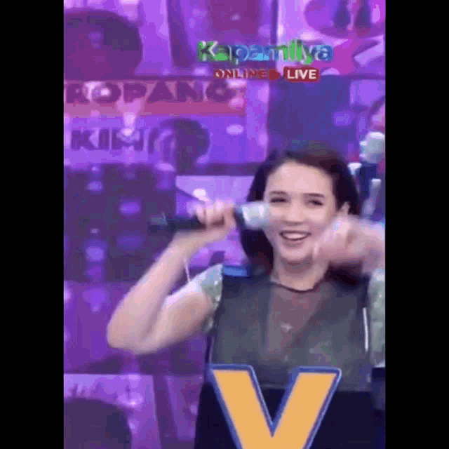 a woman is holding a microphone in front of a sign that says kapamilya