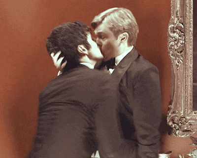 two men in suits kissing in front of a framed picture