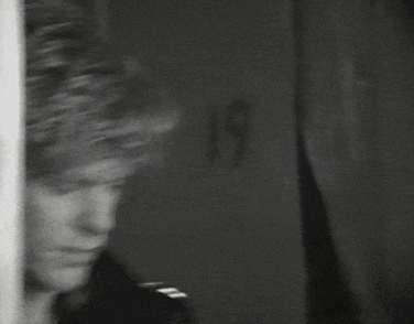 a black and white photo of a man standing in front of a wall .