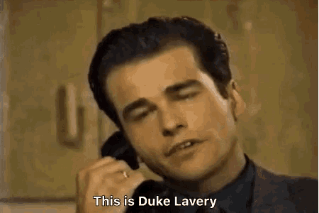 a man in a suit and tie is talking on a cell phone and saying `` this is duke lavery '' .