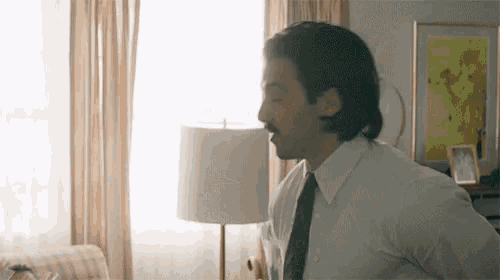 a man in a white shirt and tie is standing in a living room with a lamp .