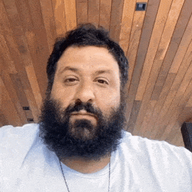 a man with a beard is wearing a white shirt and necklace
