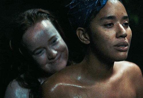 a woman with a bandana on her head is smiling next to a woman without a shirt