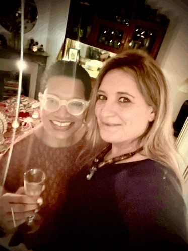 two women are standing next to each other and one is holding a glass of wine
