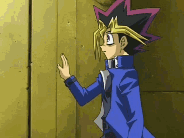a man in a blue suit is standing next to a yellow wall and touching it with his hand .