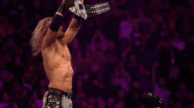 a shirtless wrestler is holding a championship belt above his head