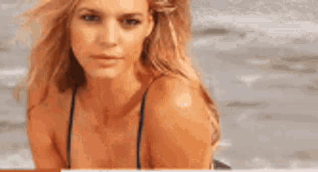 a woman in a bikini is laying on a beach looking at the camera .