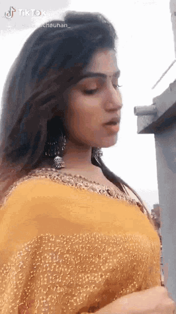 a woman is wearing a yellow top and earrings and a tiktok video